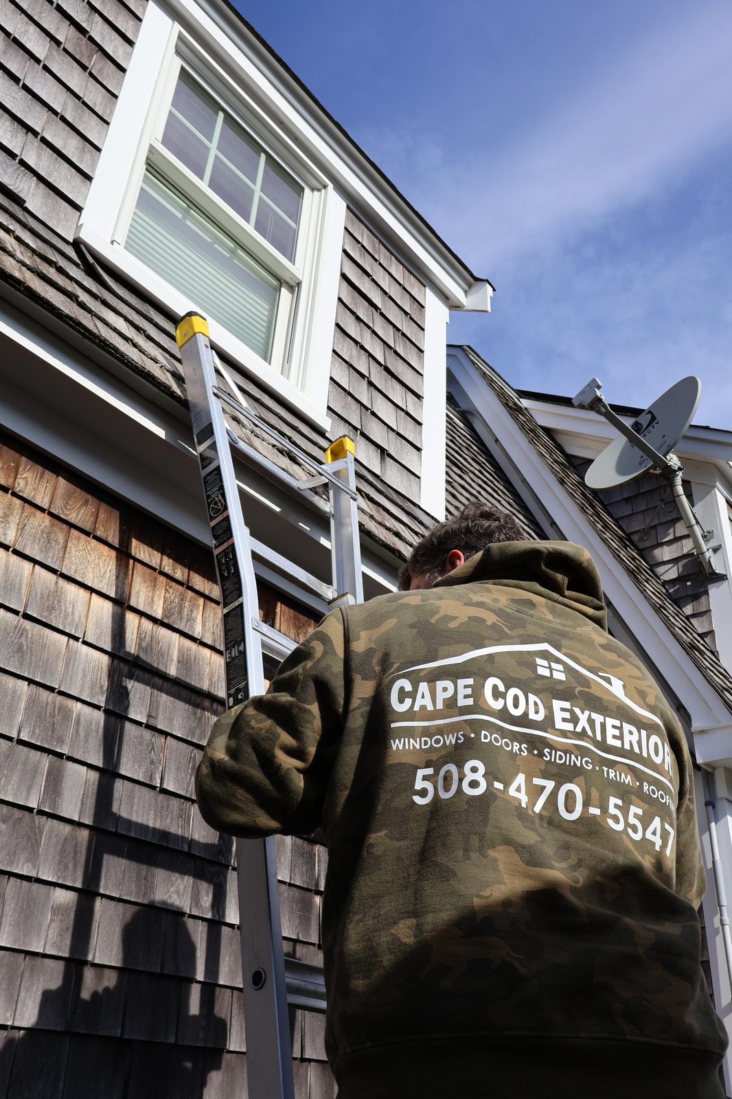 Cape Cod Exteriors crew member on ladder installing windows