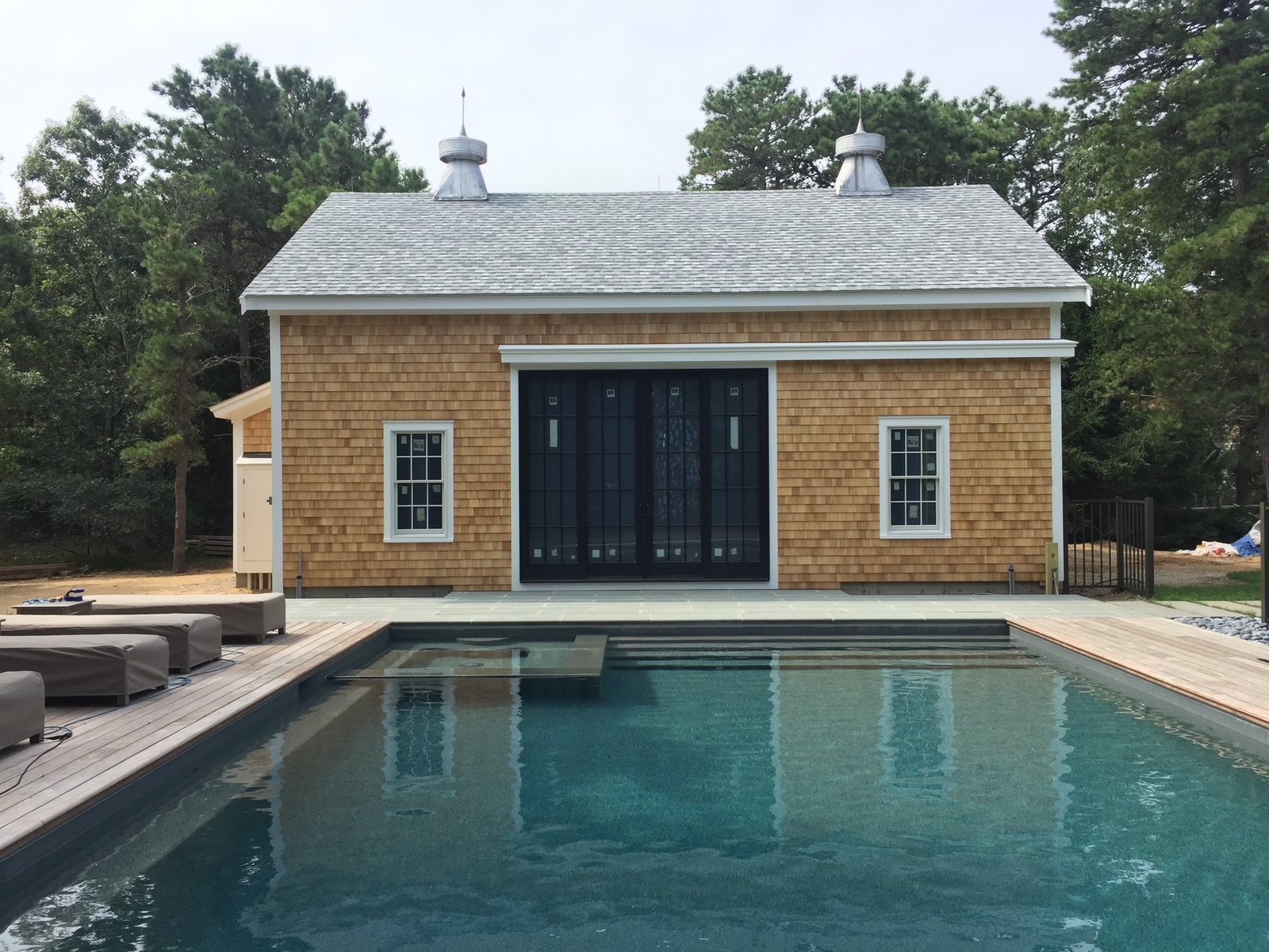 Cedar shake pool house with four-panel sliding glass door, white trim, and cupolas on Cape Cod